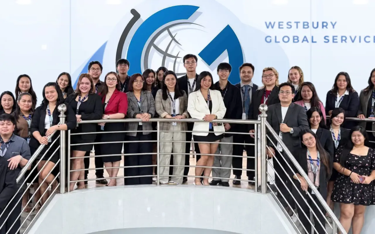 The Westbury Global Services team gathered along the staircase railings in front of the WGS feature wall